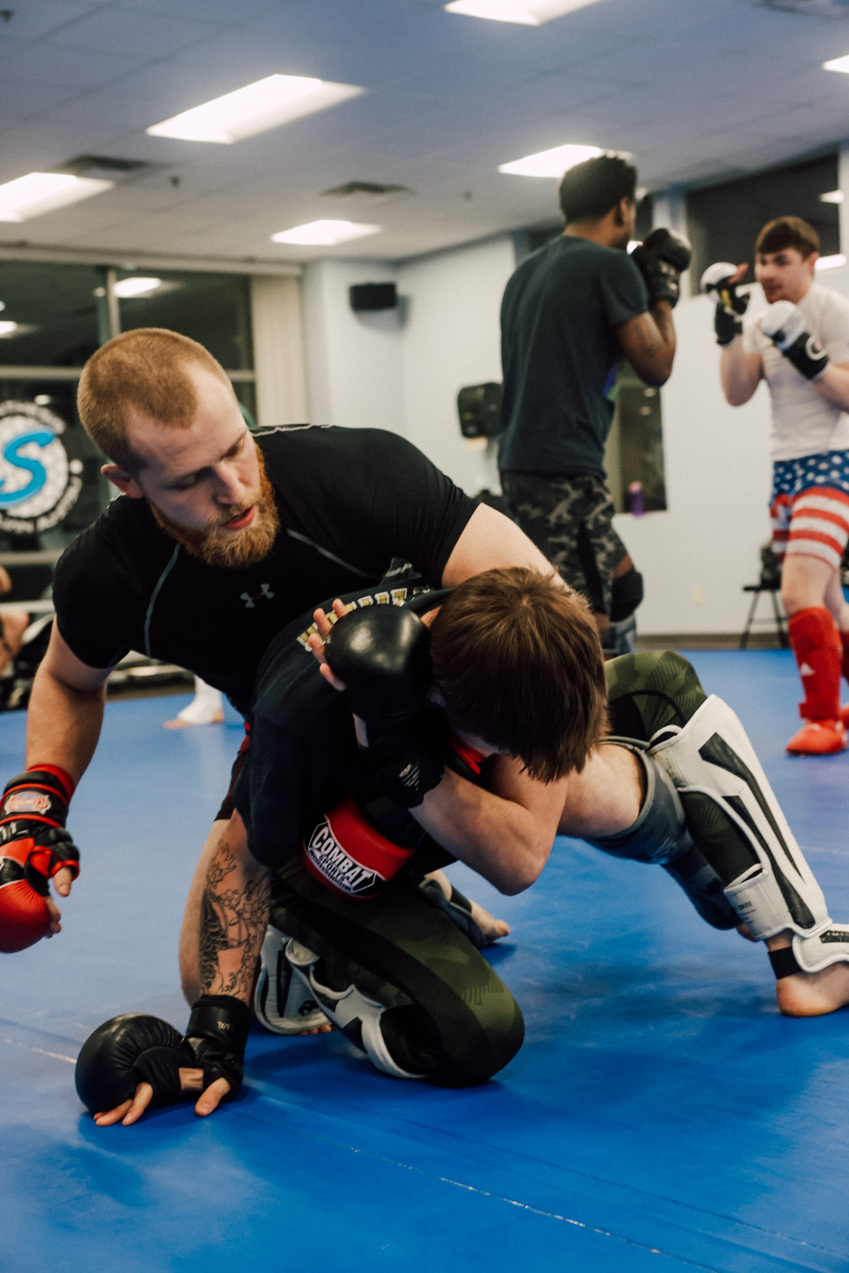 two members in sparring equipment locked in a hold on the mat