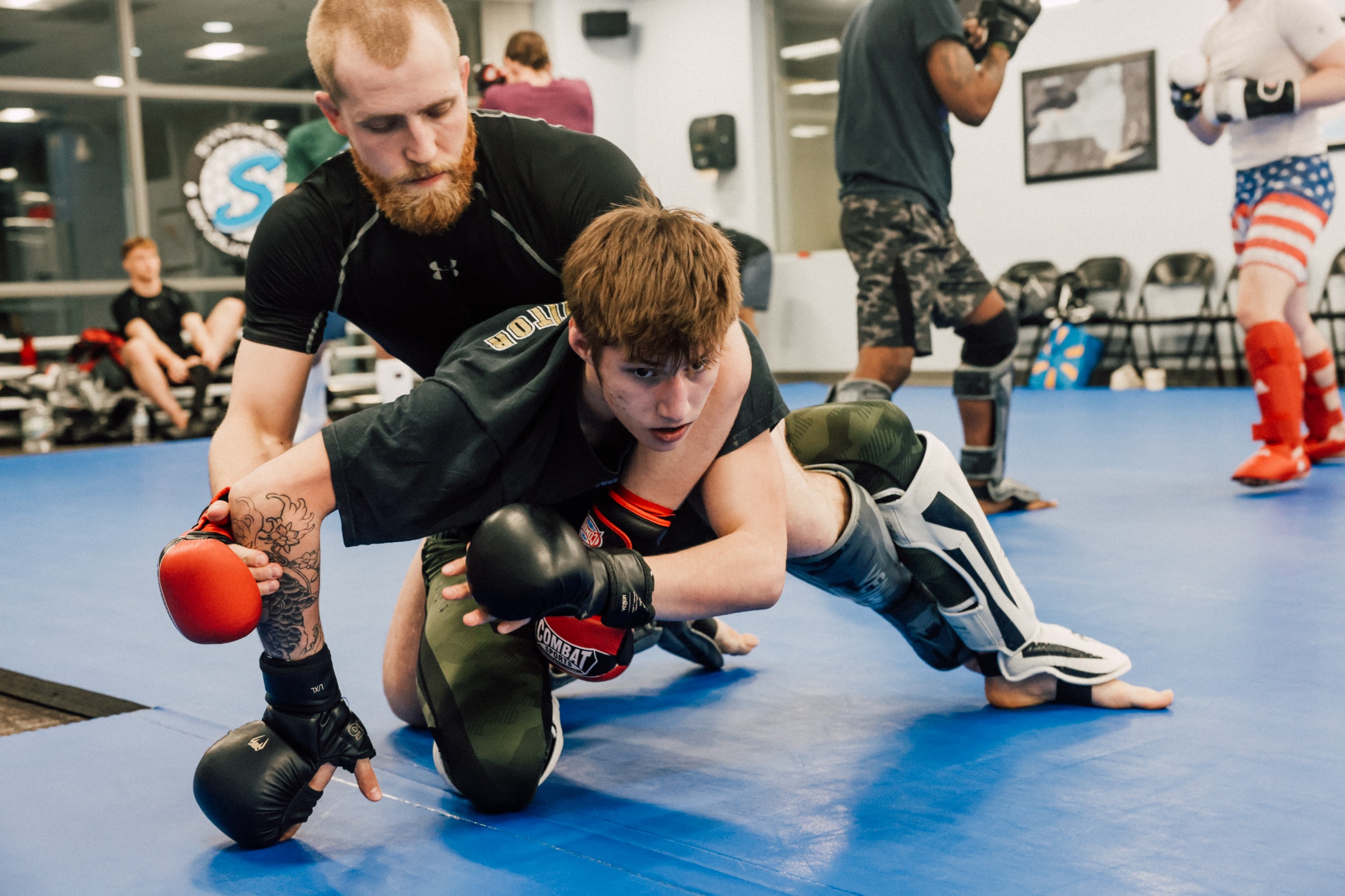 two members in sparring equipment locked in a hold on the mat